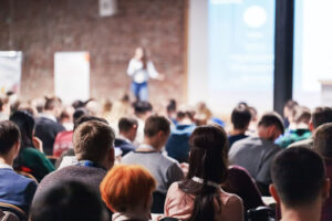 Group of people listening to a speaker on stage at a conference.