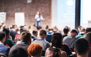 Group of people listening to a speaker on stage at a conference.
